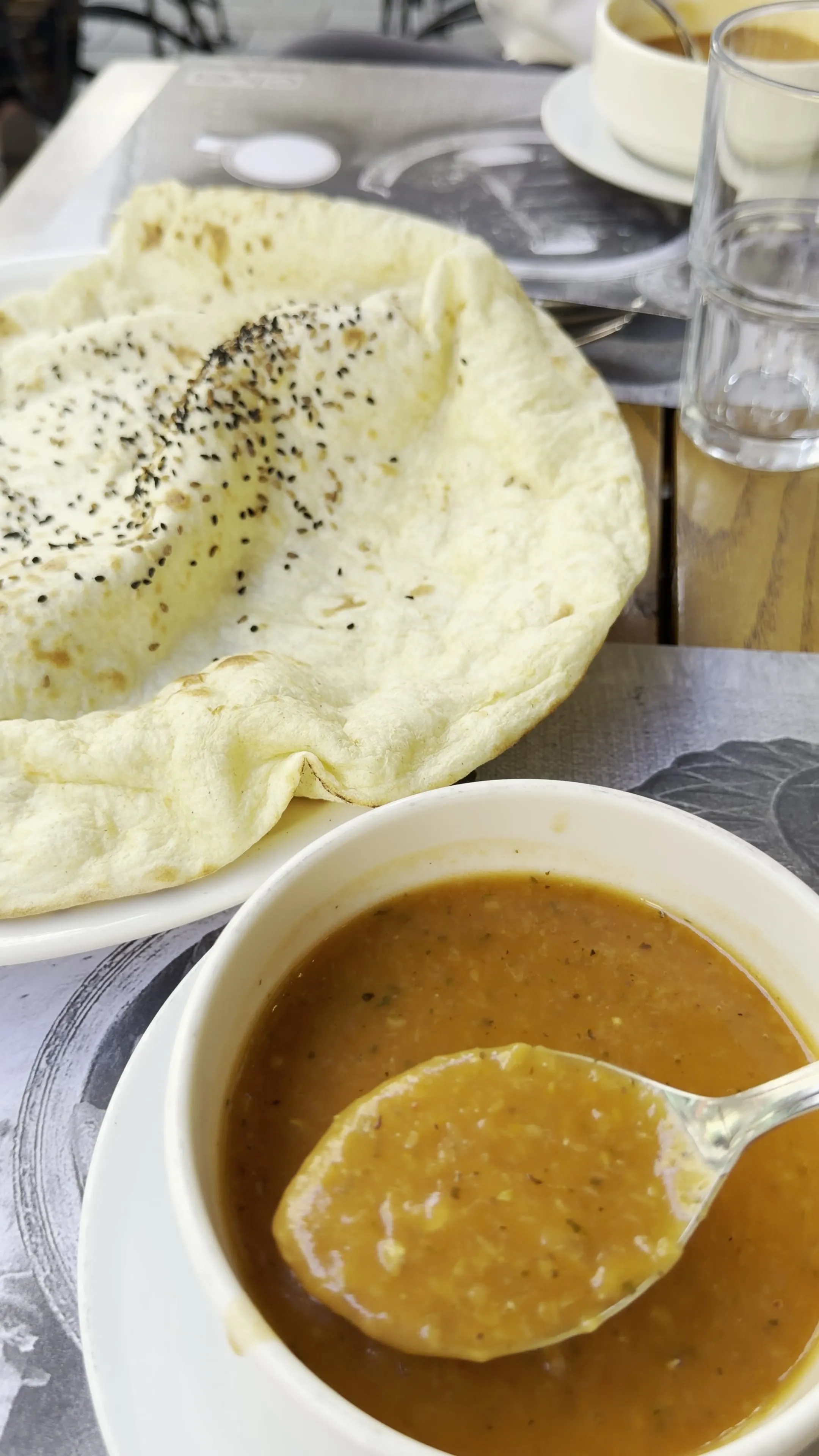 A bowl of orange lentil soup with a spoonful lifted above it, bread, and lemon