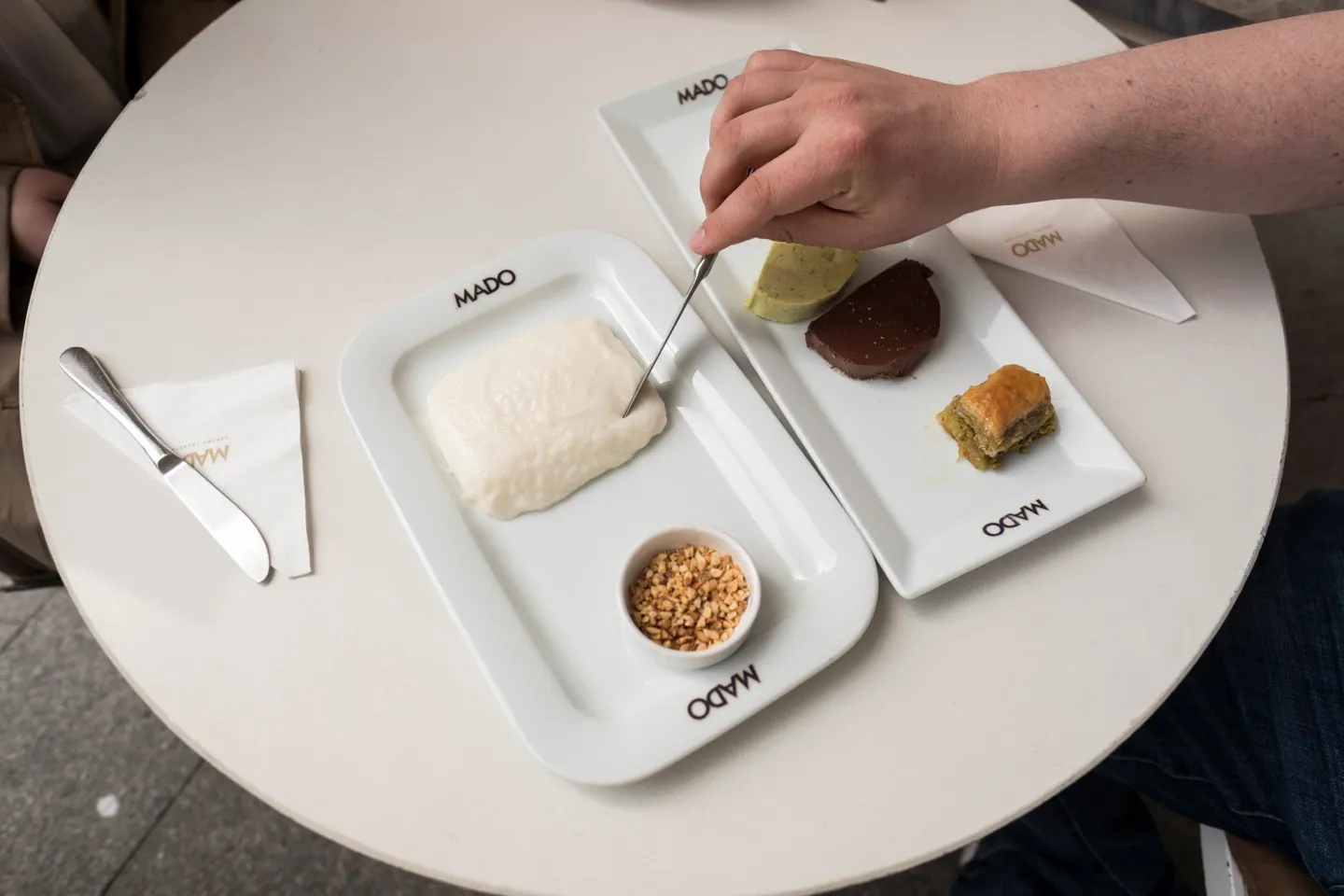 cutting a thick slab of Maras dondurma with a knife on a Mado plate, hazelnuts on the side