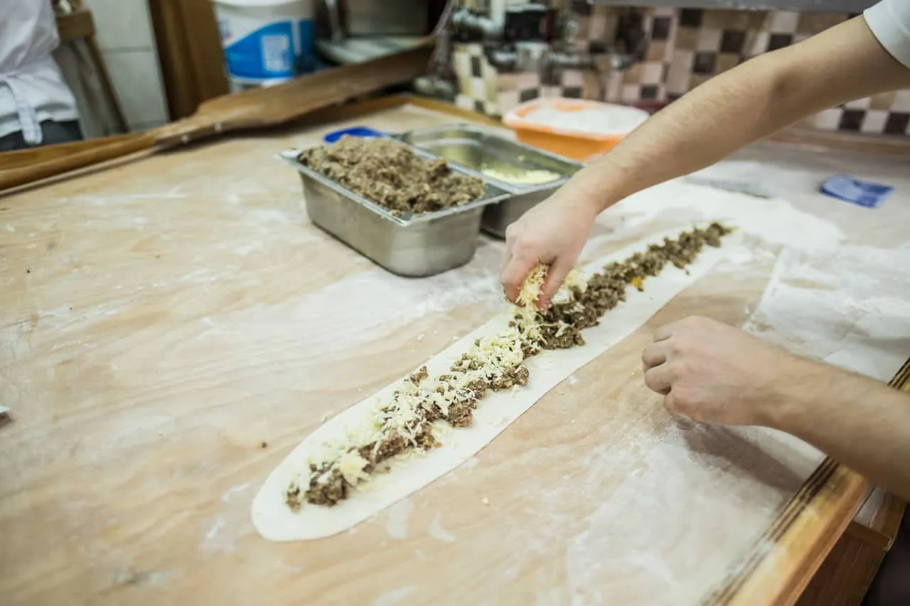 Long pide dough on a wooden bench being filled with cheese and minced meat