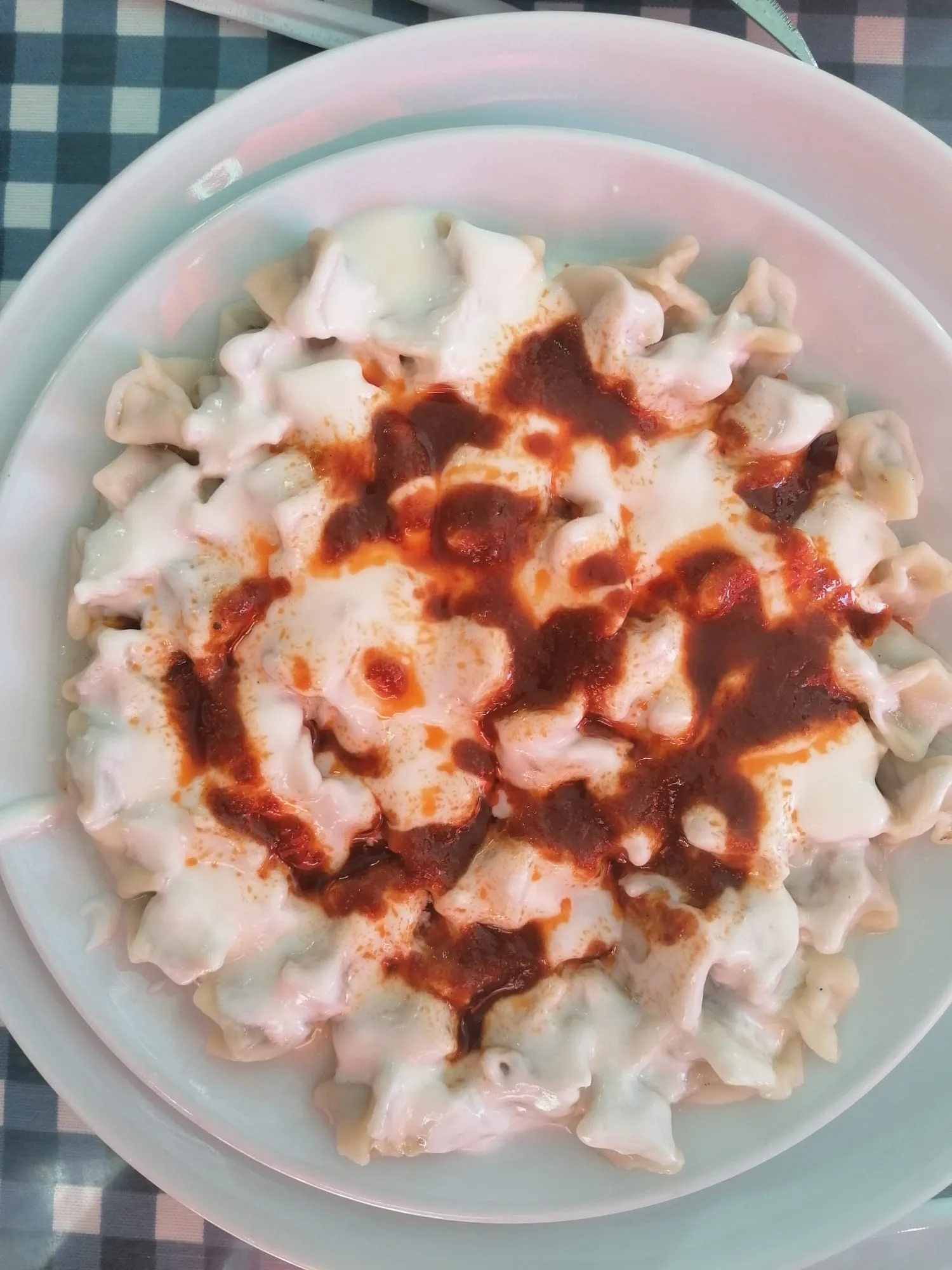 Plate of mantı dumplings under yogurt with red pepper butter spooned over the top