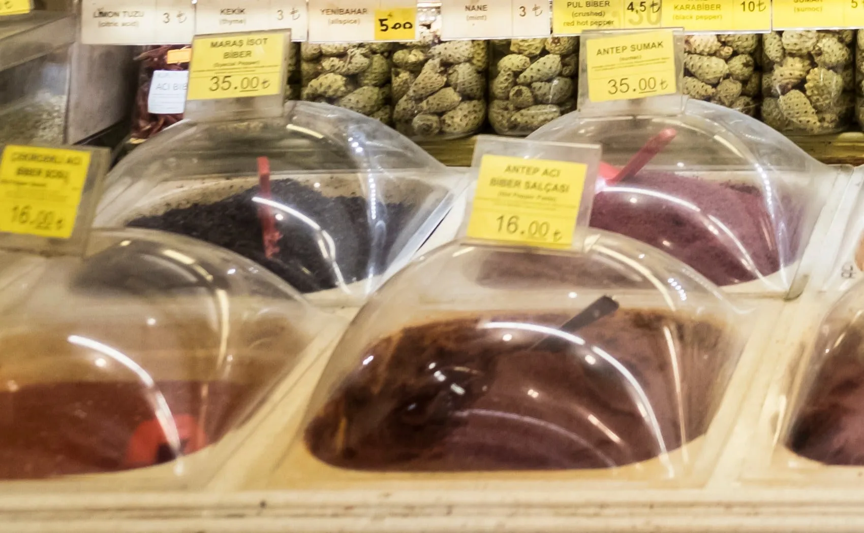 Handwritten price tag reading Maraş isot biber above open bins of dark pepper flakes in an Istanbul shop