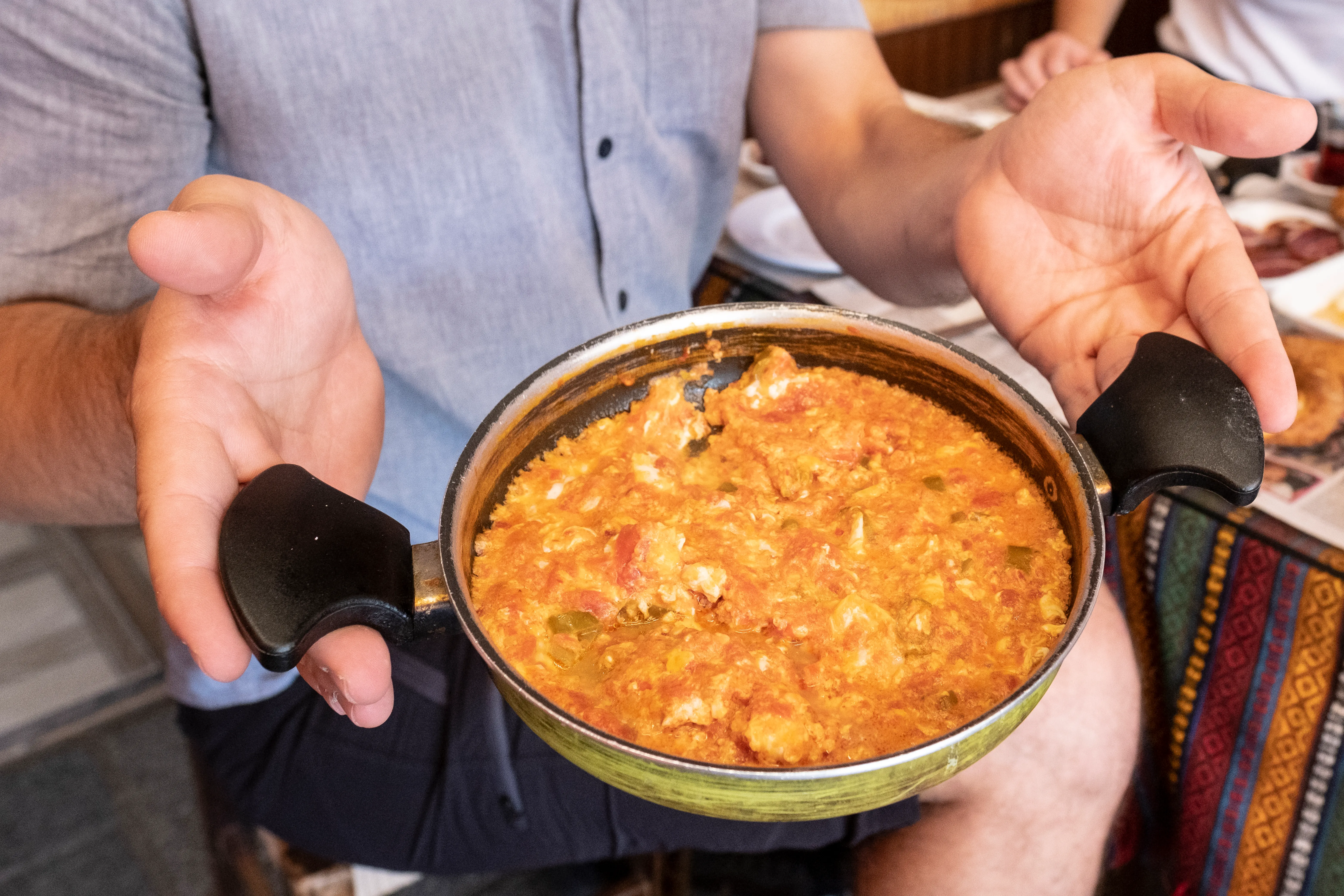 A shallow pan of menemen held above a breakfast table