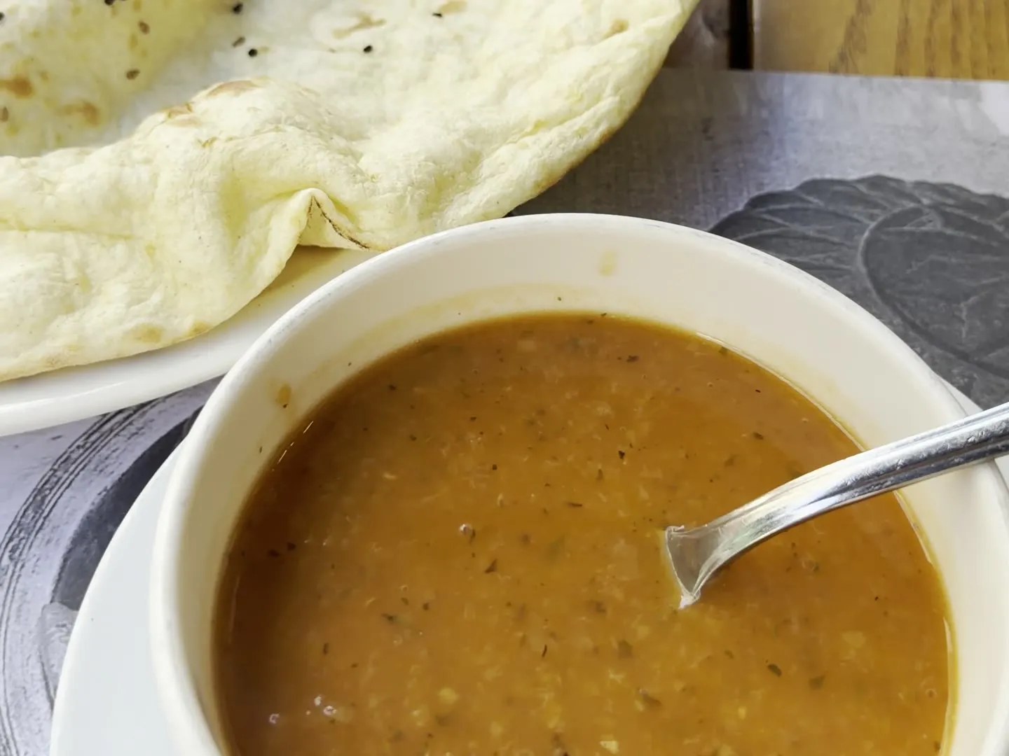 A bowl of mercimek çorbası with a spoon, next to a puffed seeded lavash