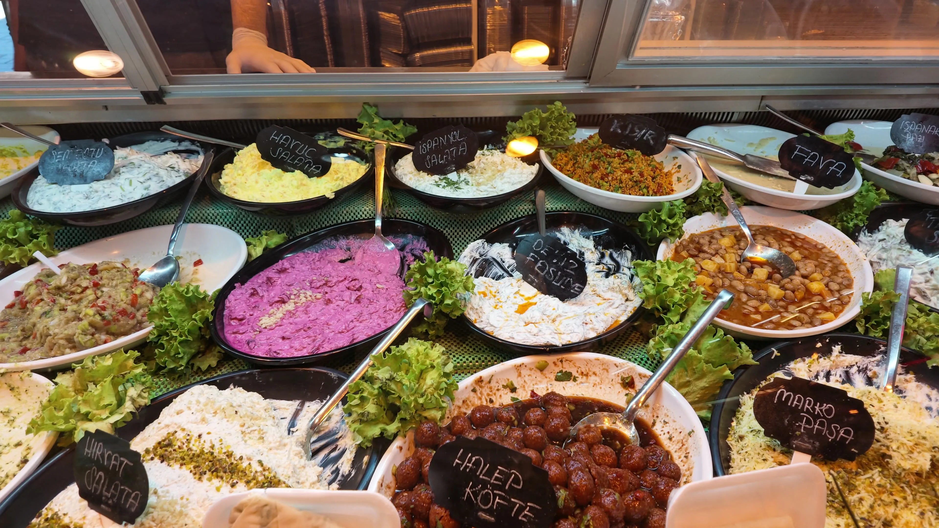 A chilled counter filled with colorful trays of prepared meze