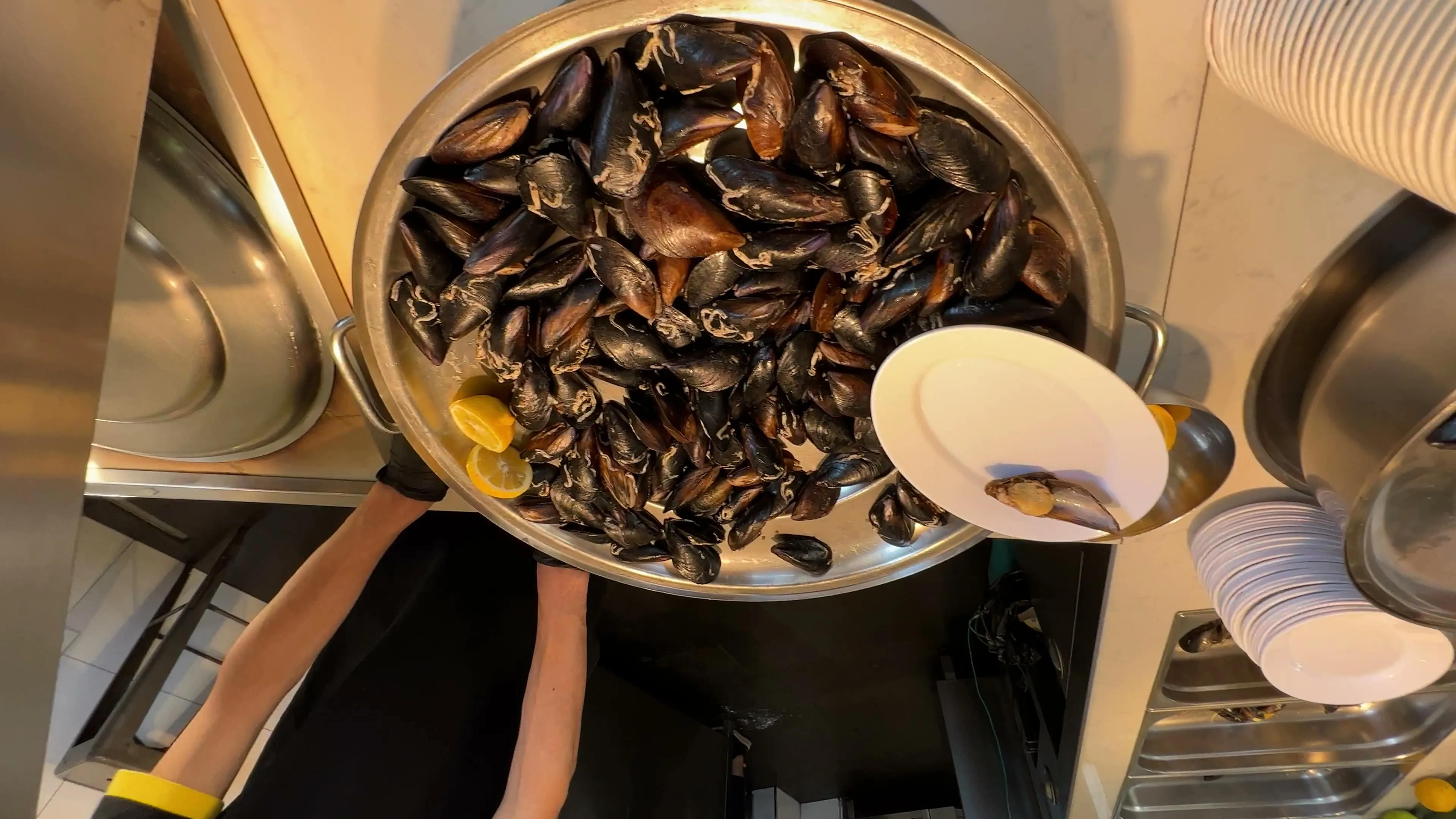 A large tray of mussel shells, opened stuffed mussels, and lemon beside a serving plate