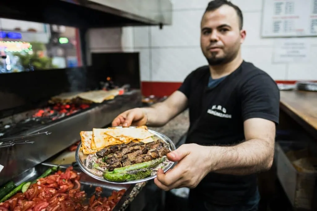 Chef in front of char grill offering plate of kebab with rice, peppers, flat bread on food tour