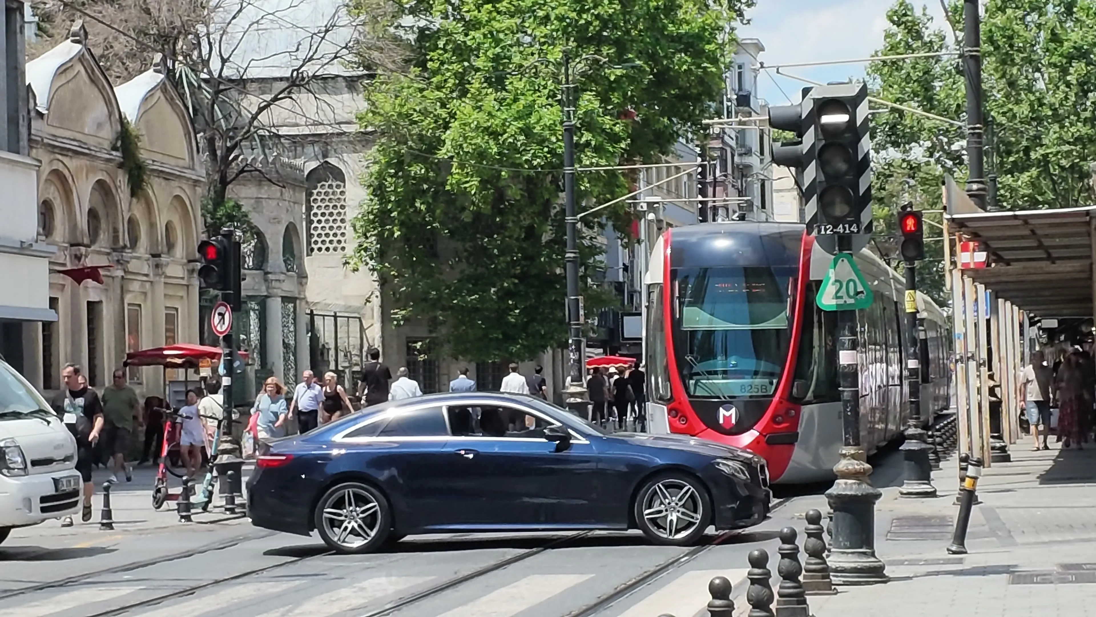 A modern red-and-silver tram passes stone buildings, pedestrians, and traffic in Istanbul