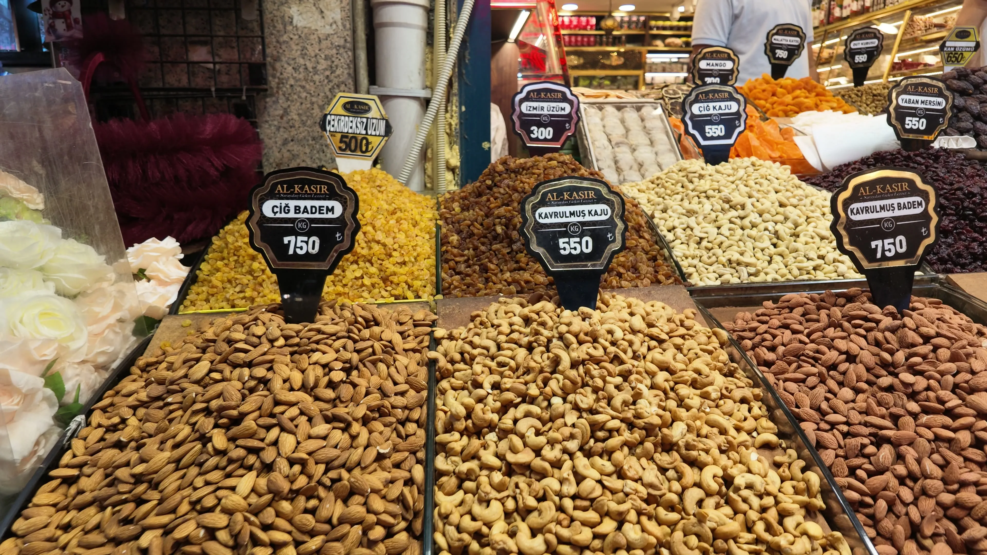 Open bins of almonds and cashews with Turkish labels at a market counter