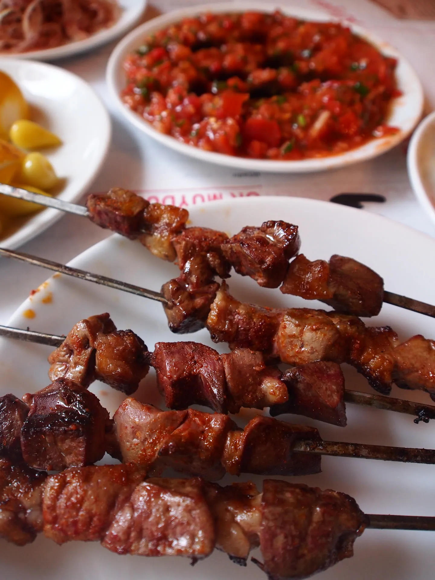 grilled lamb skewers on a plate beside ezme, pickled peppers and sumac onions