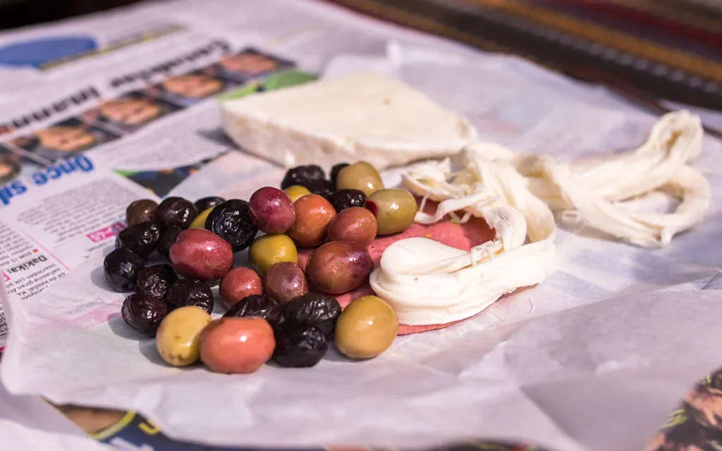 Green and black olives beside white and string cheeses on paper