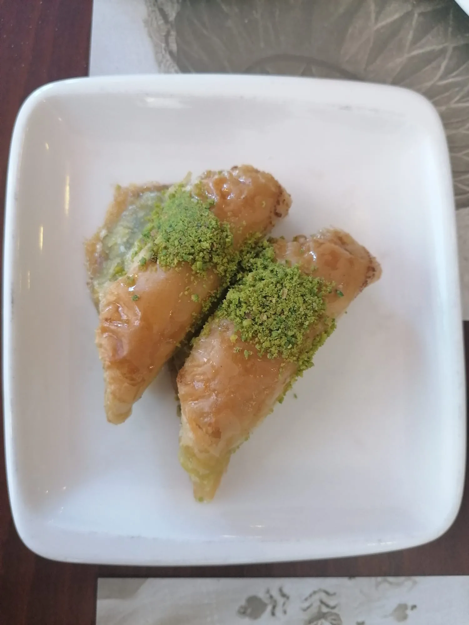 Two triangular pieces of layered baklava topped with ground pistachios on a white plate