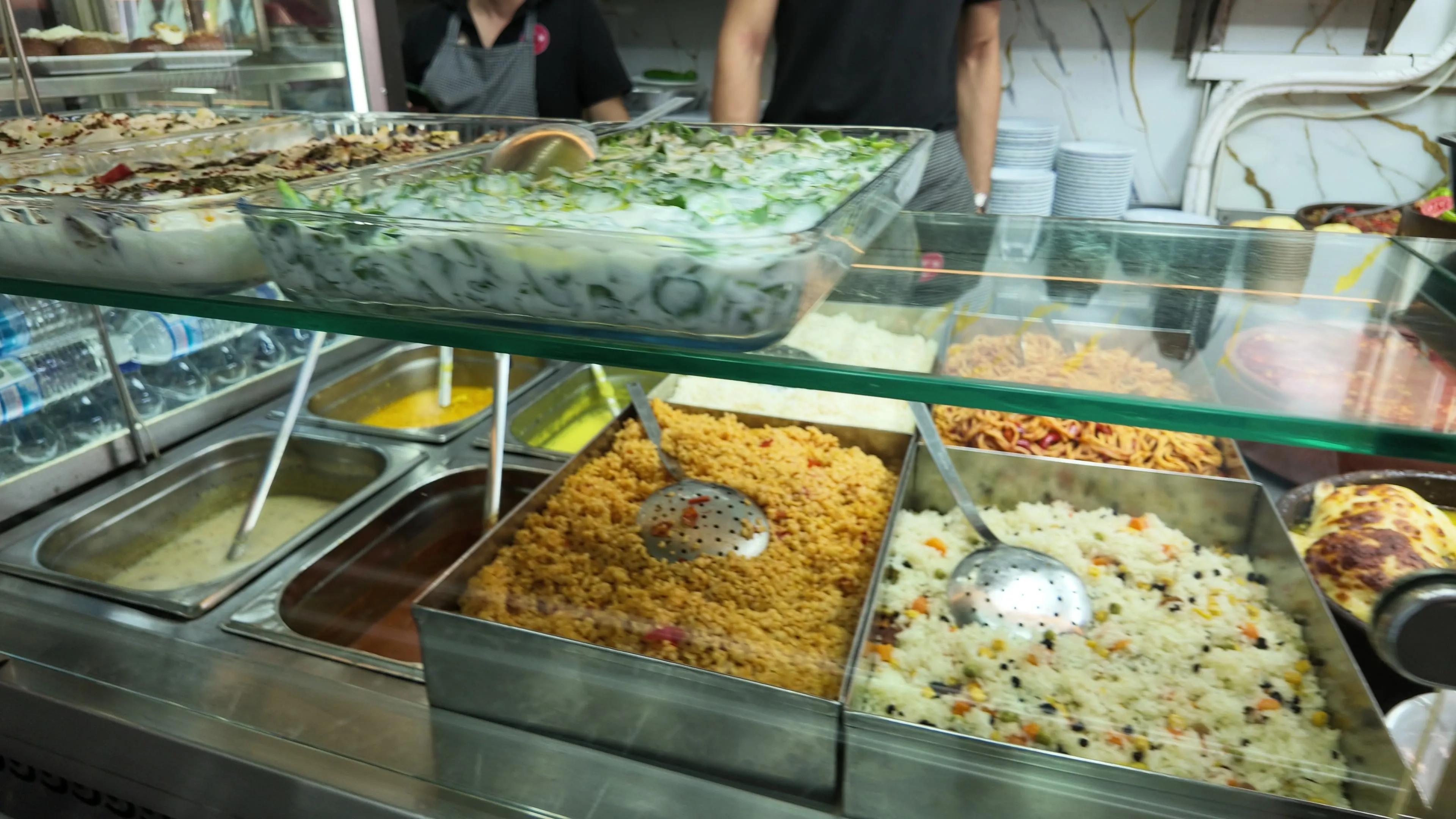 Trays of rice, vegetables, and creamy salads behind a glass serving counter