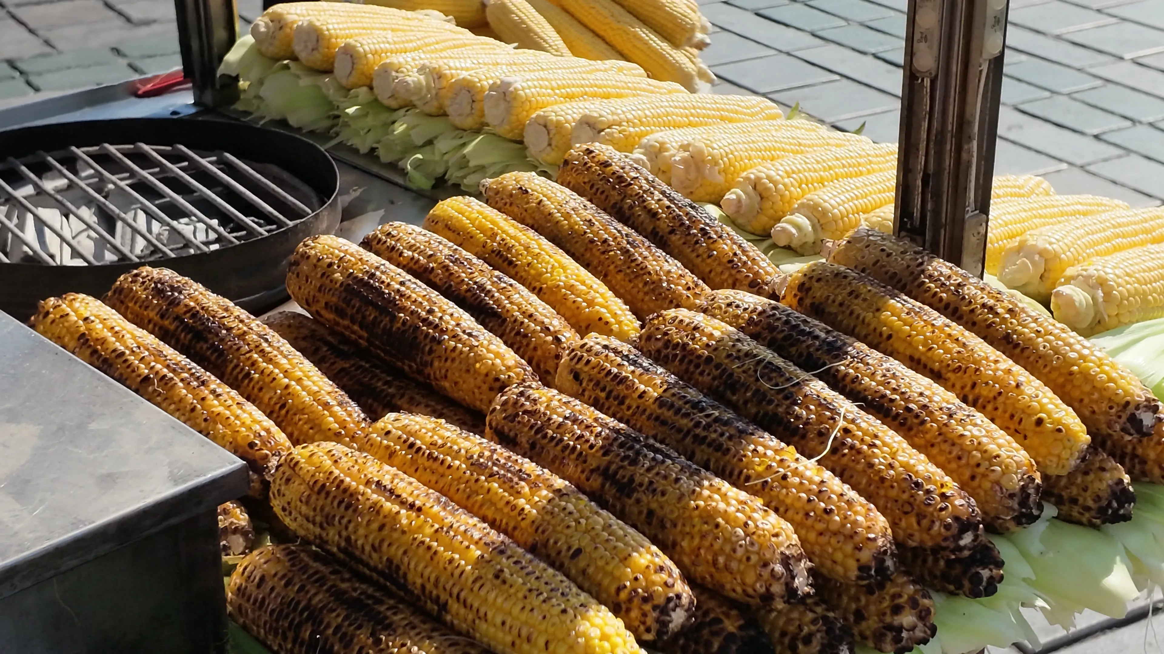 Rows of charred corn on the cob displayed beside the grill of a street cart