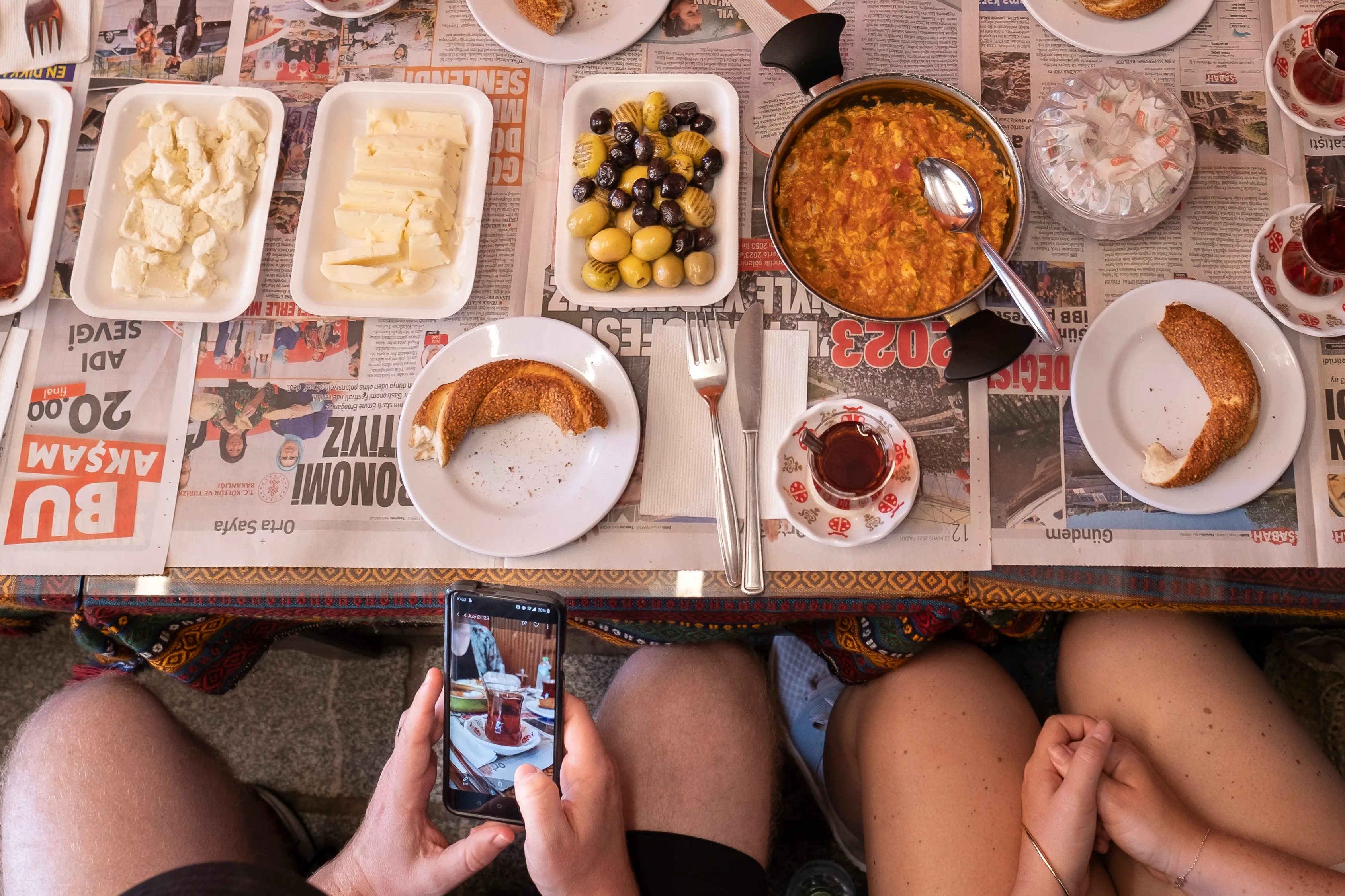 An overhead Turkish breakfast spread with menemen, simit, cheeses, olives, and tea
