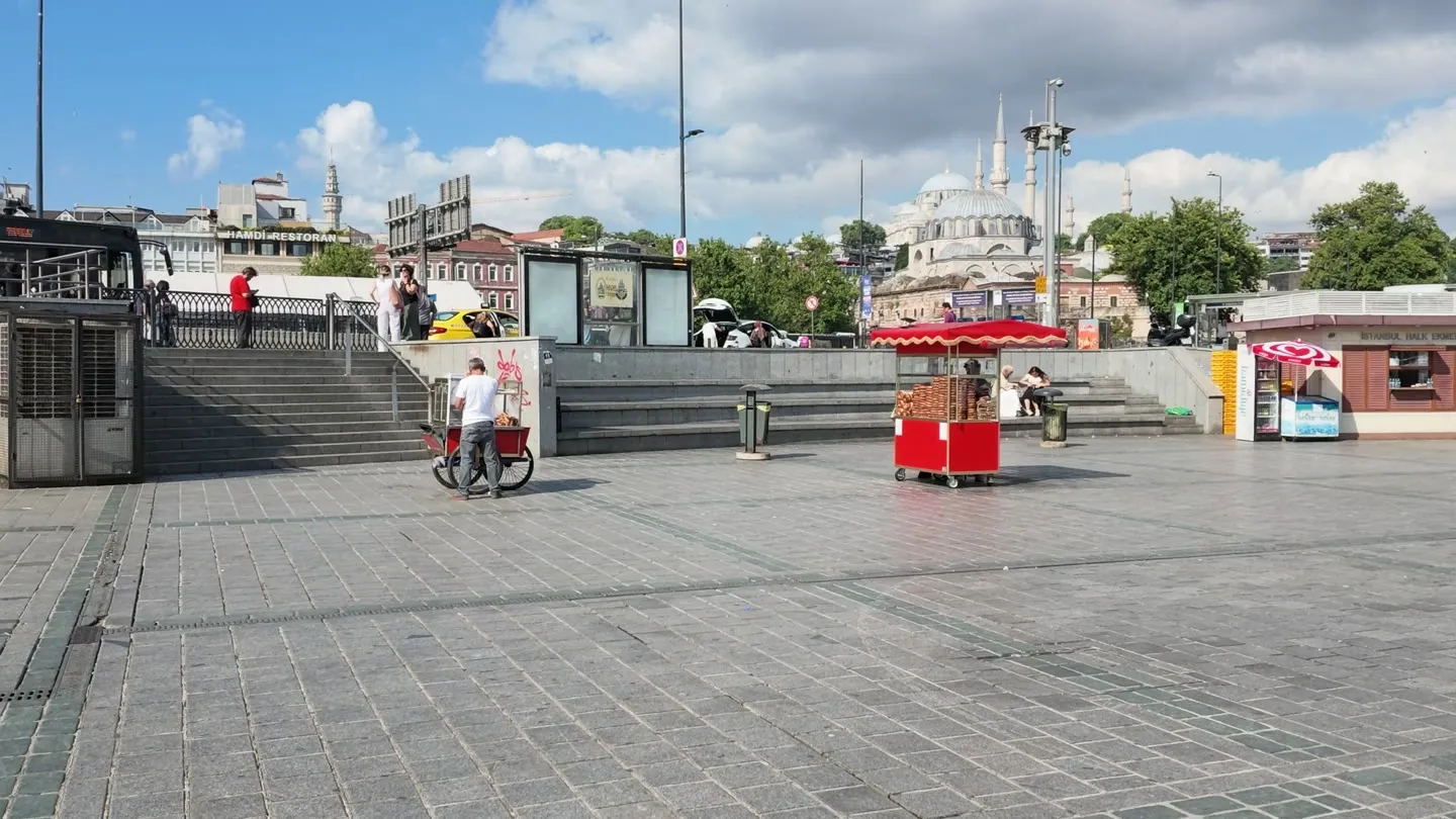 A red simit cart on the square at Eminönü with a mosque on the skyline behind it