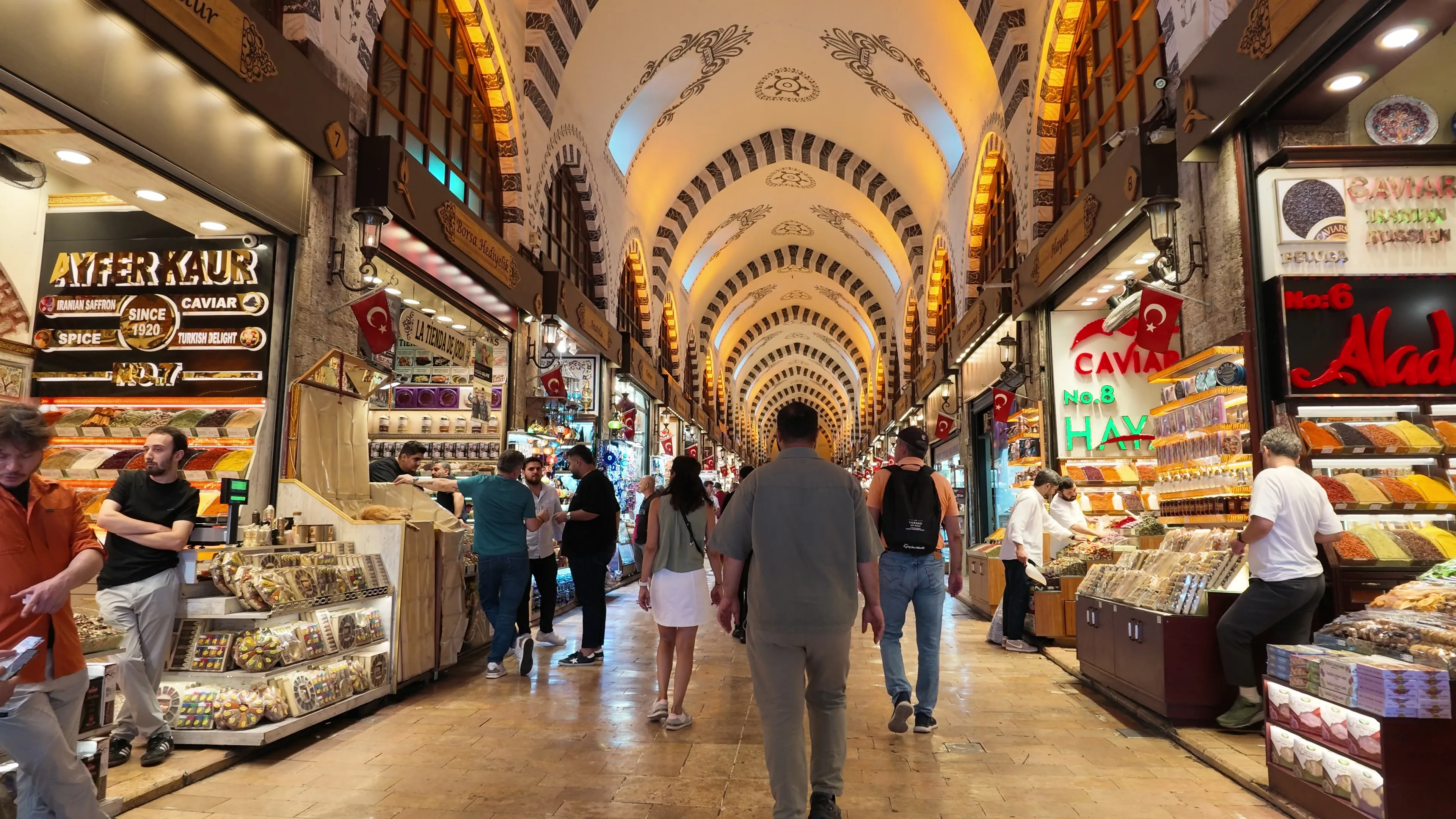 Shoppers walk between spice and confectionery shops beneath the patterned vaults of the Spice Bazaar