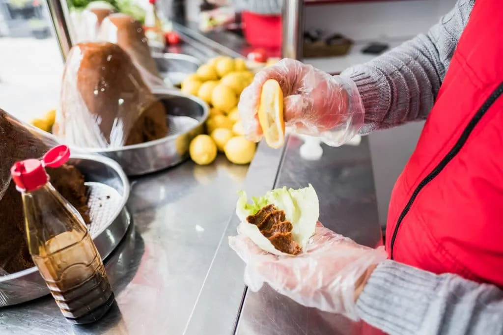 çiğ köfte vendor wearing plastic gloves while squeezing lemon over meatball wrapped in lettuce leaf, street food