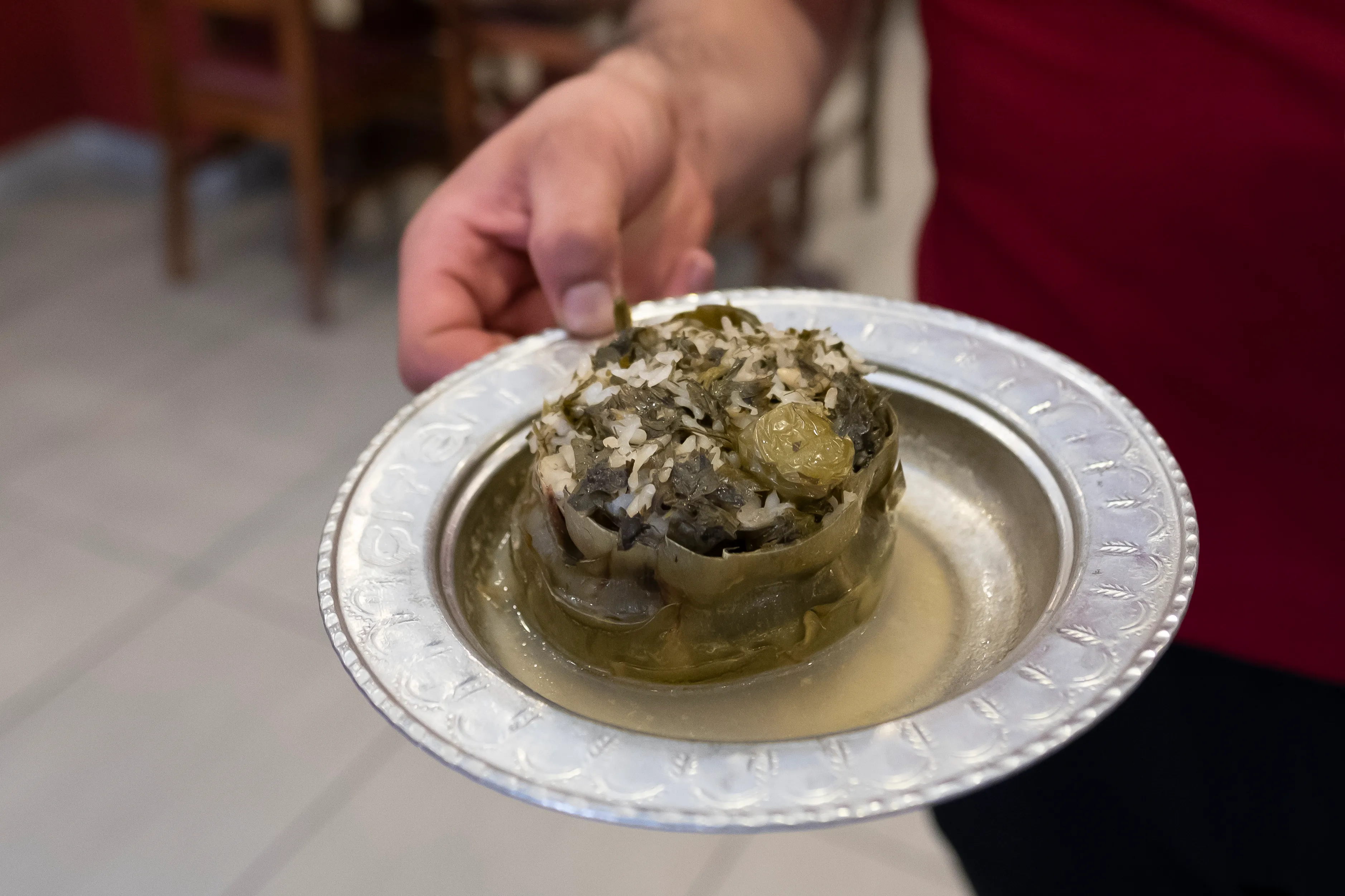 A stuffed artichoke with herbs served on an ornate silver plate
