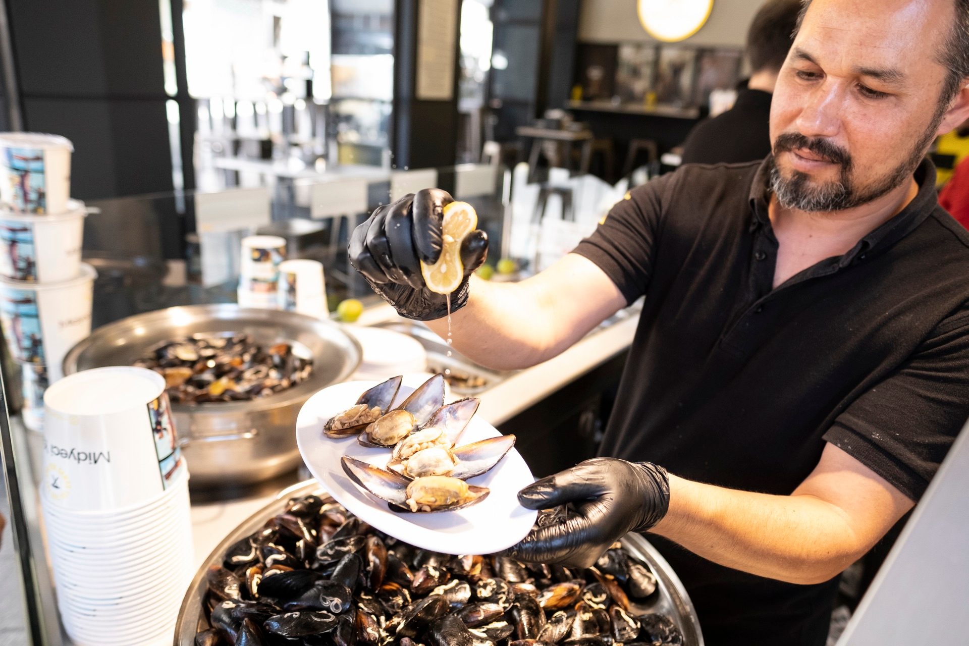 Gloved vendor squeezing lemon over a plate of stuffed mussels, midye dolma, in Kadıköy, Istanbul