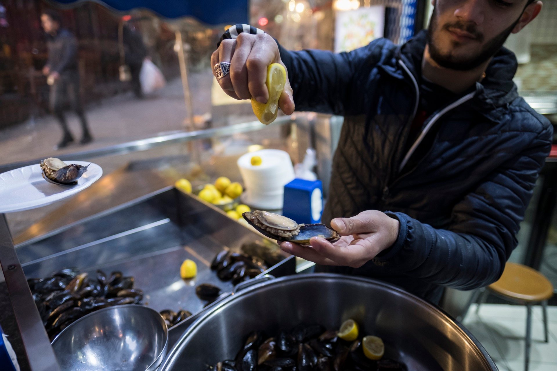 Vendor squeezing lemon over a stuffed mussel, midye dolma, at a street counter in Istanbul