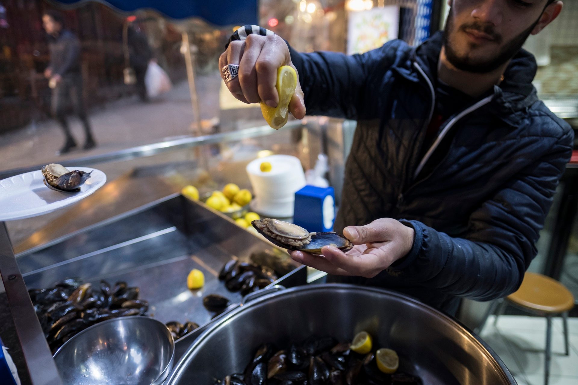 Vendor squeezing lemon over a stuffed mussel, midye dolma, at a street counter in Istanbul