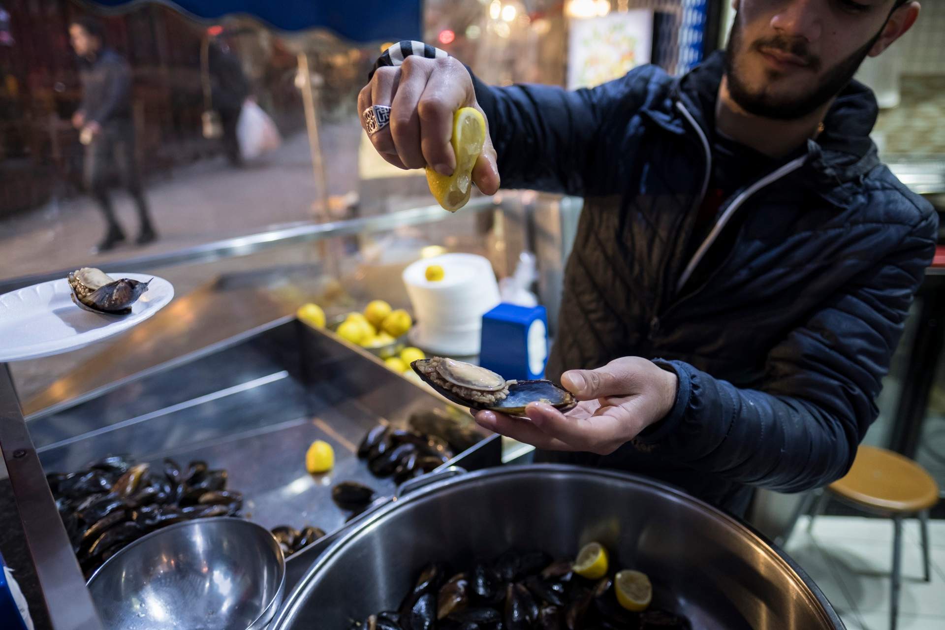 Vendor squeezing lemon over a stuffed mussel, midye dolma, at a street counter in Istanbul