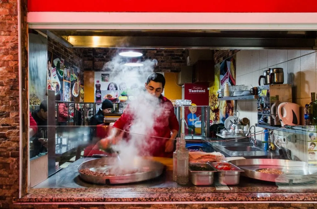 Chef cooking tantuni on circular metal stove causing steam to float through kitchen two continents food tour
