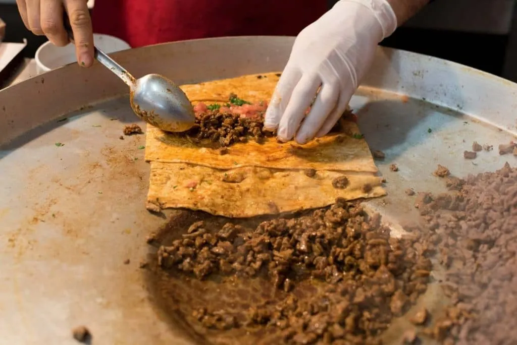 chef preparing tantuni. placing chopped beef meat inside a lavash bread with tomatoes and parsley