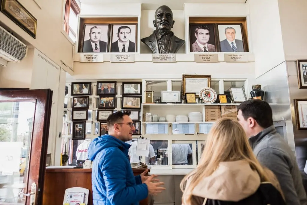 Tour guide and 2 guests talking at restaurant counter photos of previous owners guests in background
