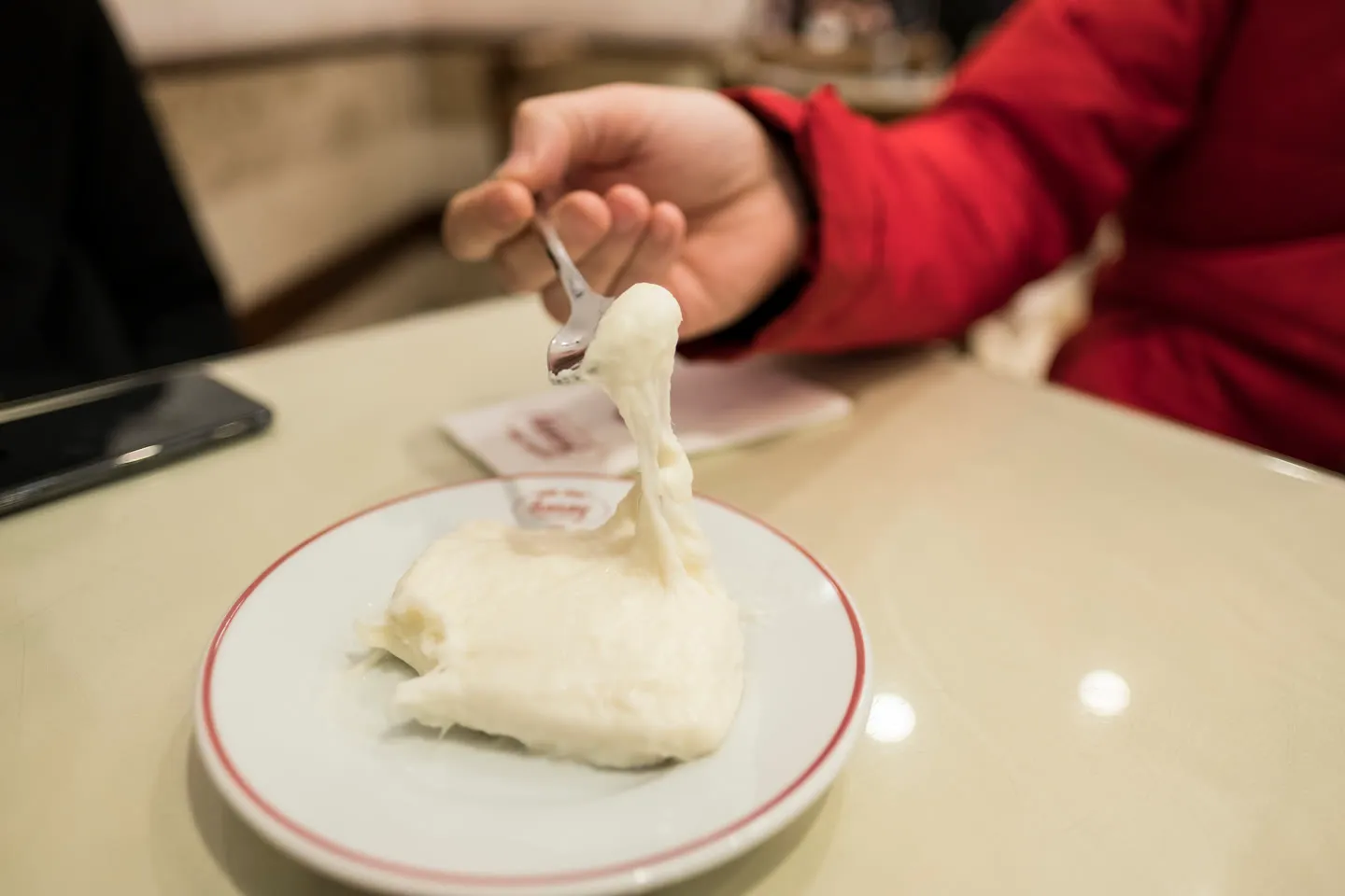 a fork lifting a stretchy ribbon from a white slab of tavuk gogsu milk pudding on a plate