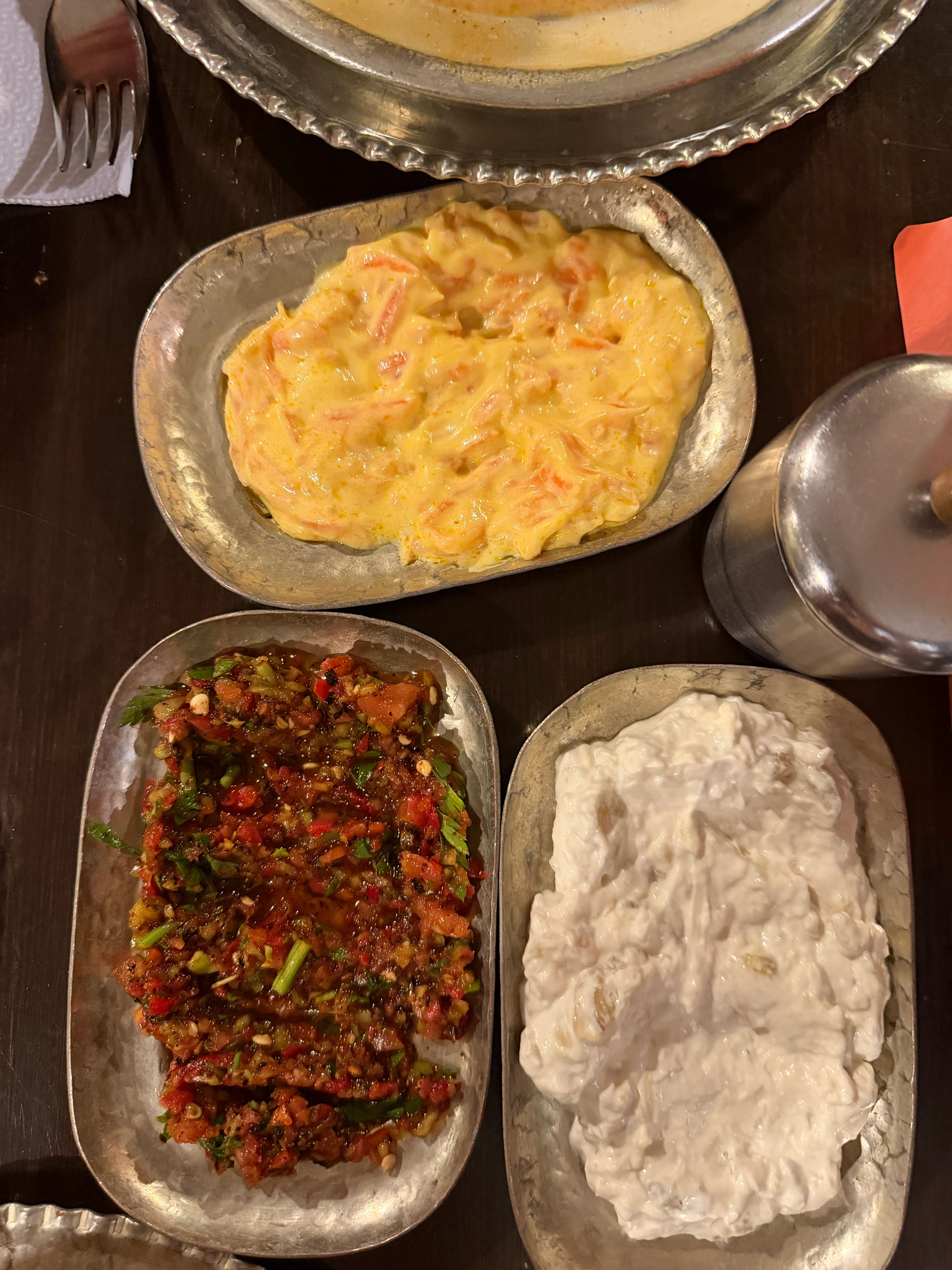 Three small metal dishes contain a red chopped mixture, a pale creamy meze, and a yellow-orange meze