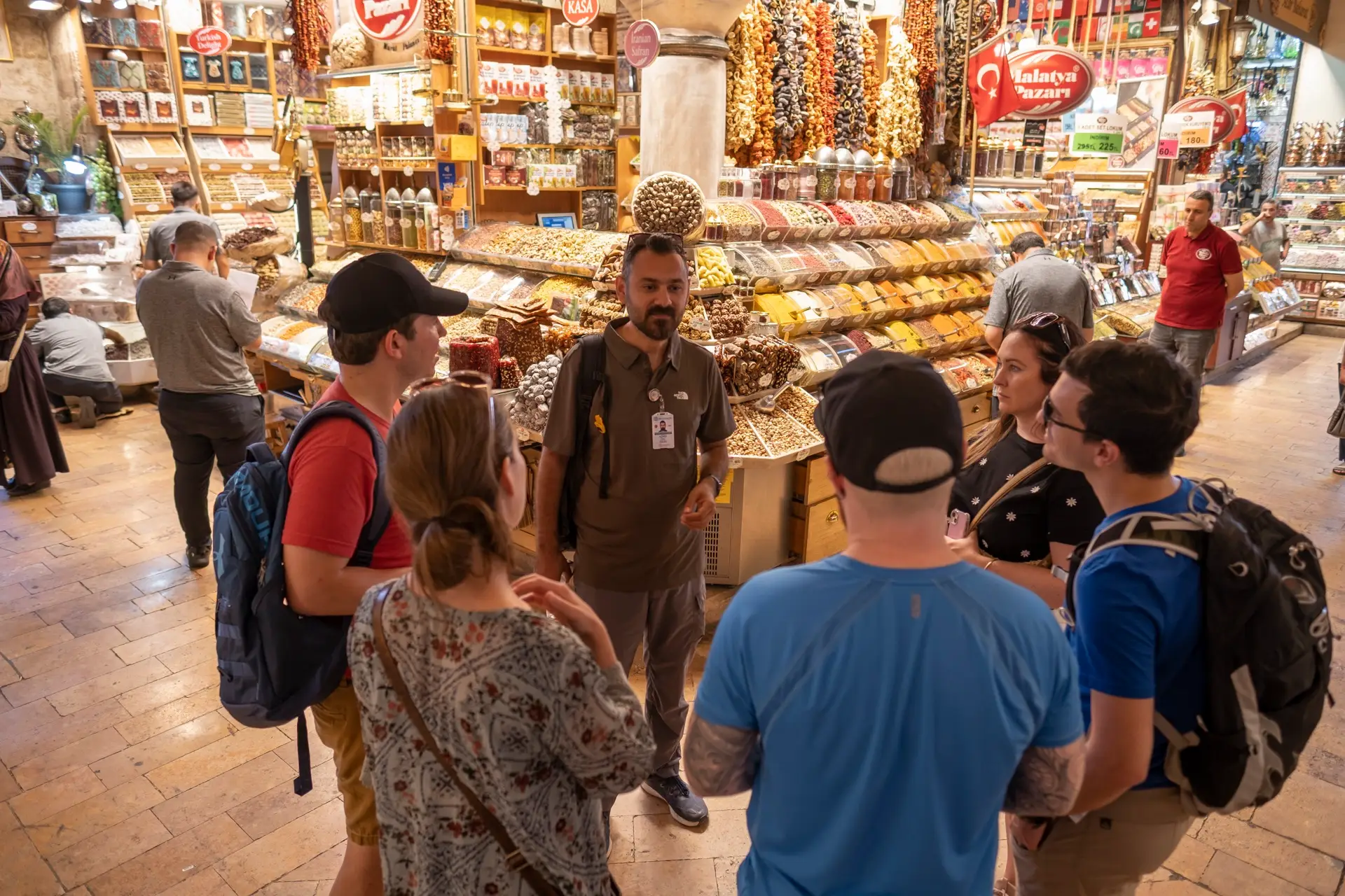 Tour guide explaining to a group of guests inside the Istanbul Spice Bazaar, surrounded by spice and dried-fruit displays
