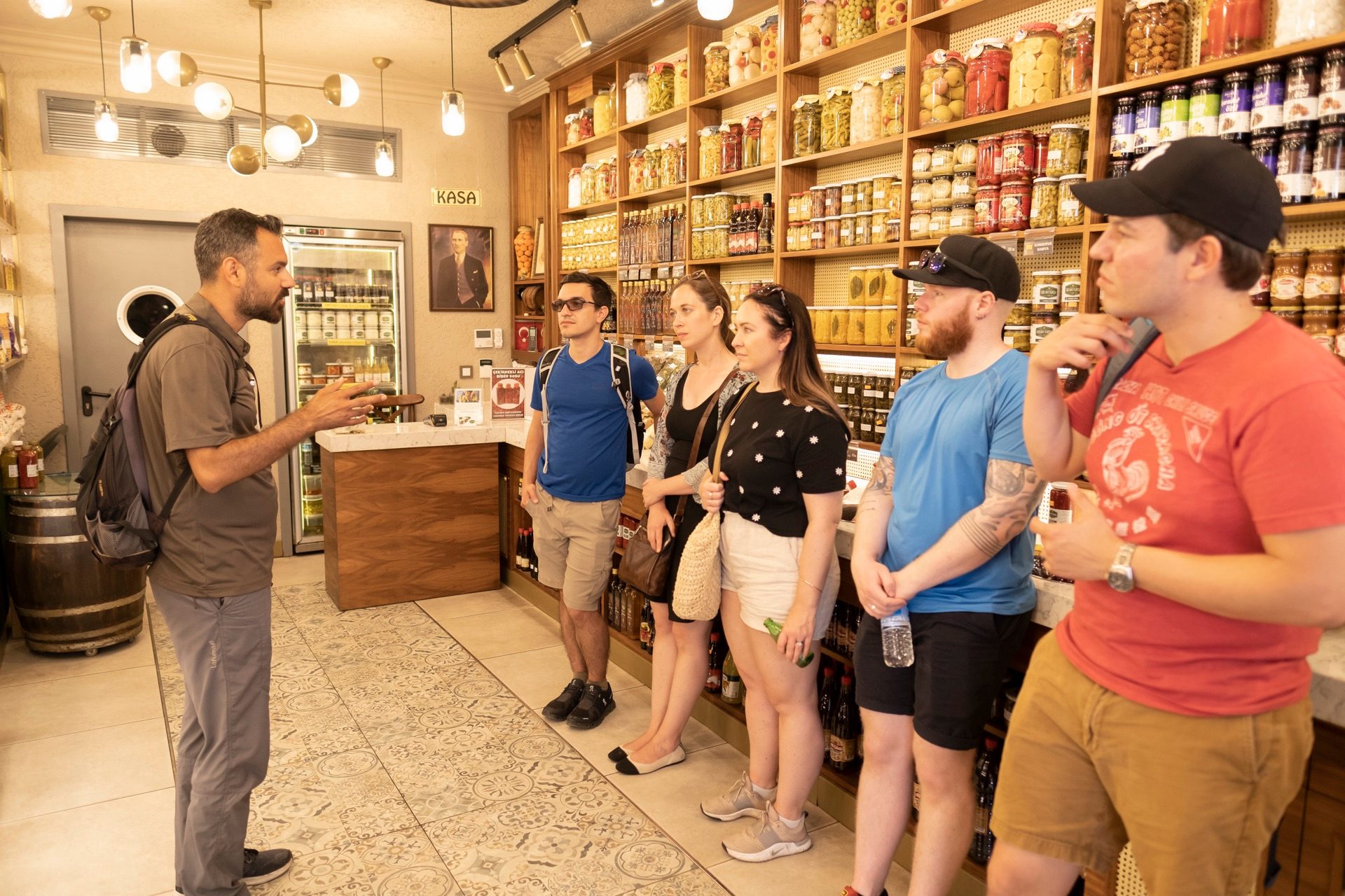 Guide talking to guests inside a Kadıköy delicatessen with jar-lined shelves in Istanbul