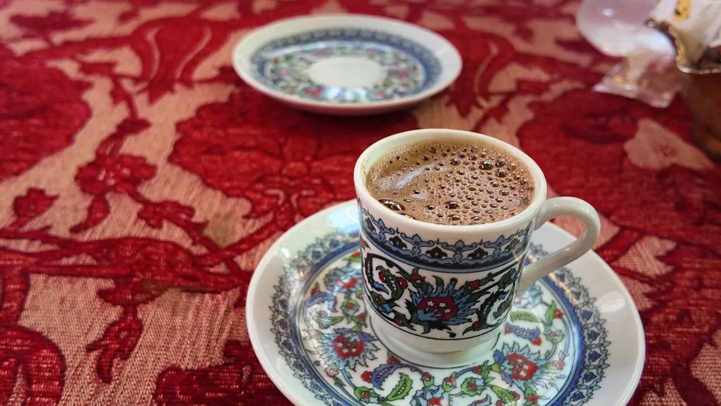 Turkish coffee with a thick foam in an Iznik-patterned cup and saucer on a red cloth