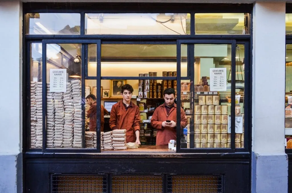 Sellers in red jackets standing inside famous coffee roaster shop surrounded by tins of turkish coffee