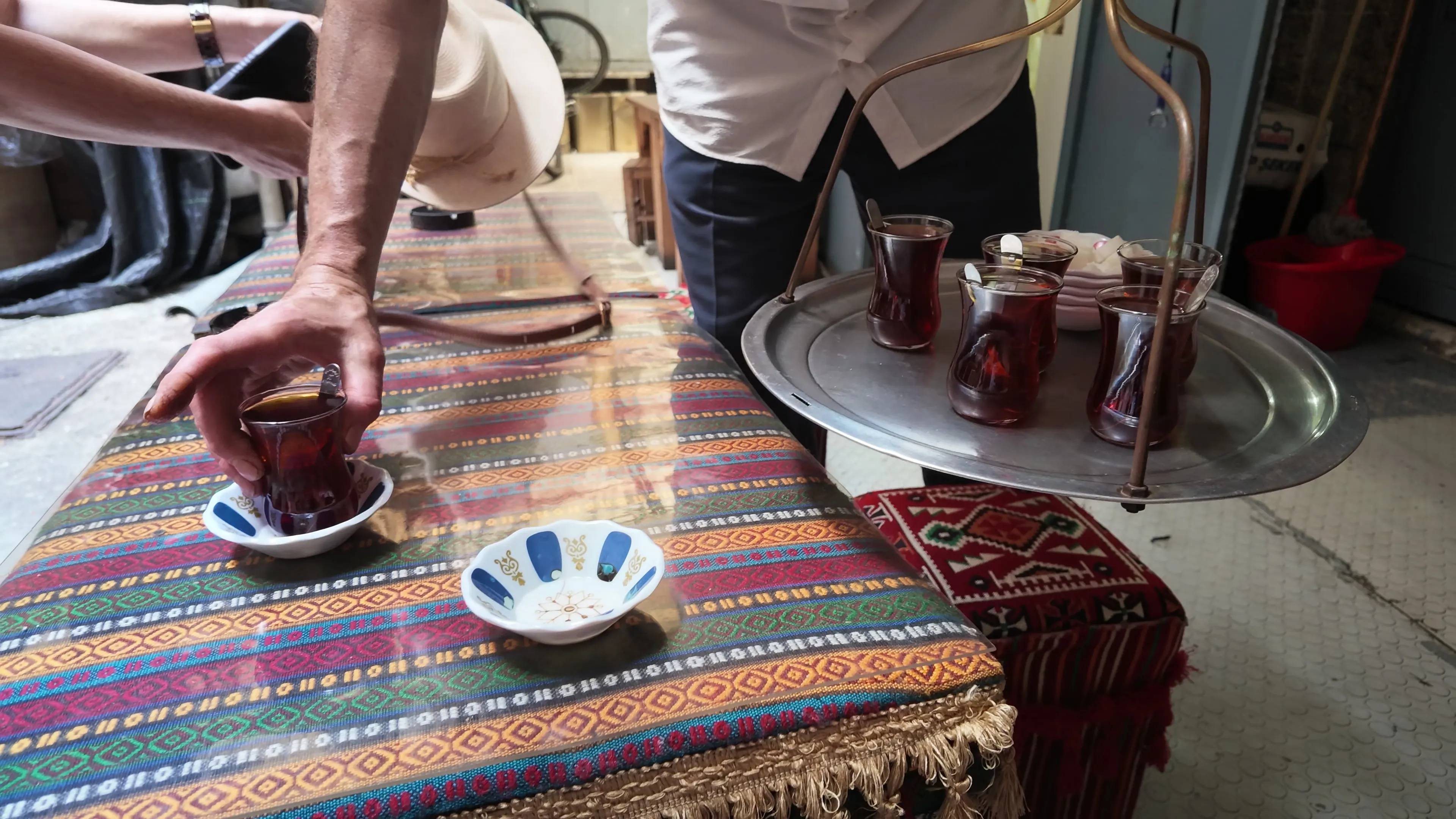 A server sets a tulip-shaped glass of Turkish tea on a patterned tablecloth